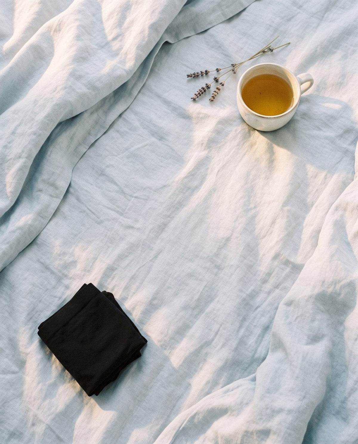 Kiri Selene Black nightwear folded on airy blue linen with tea