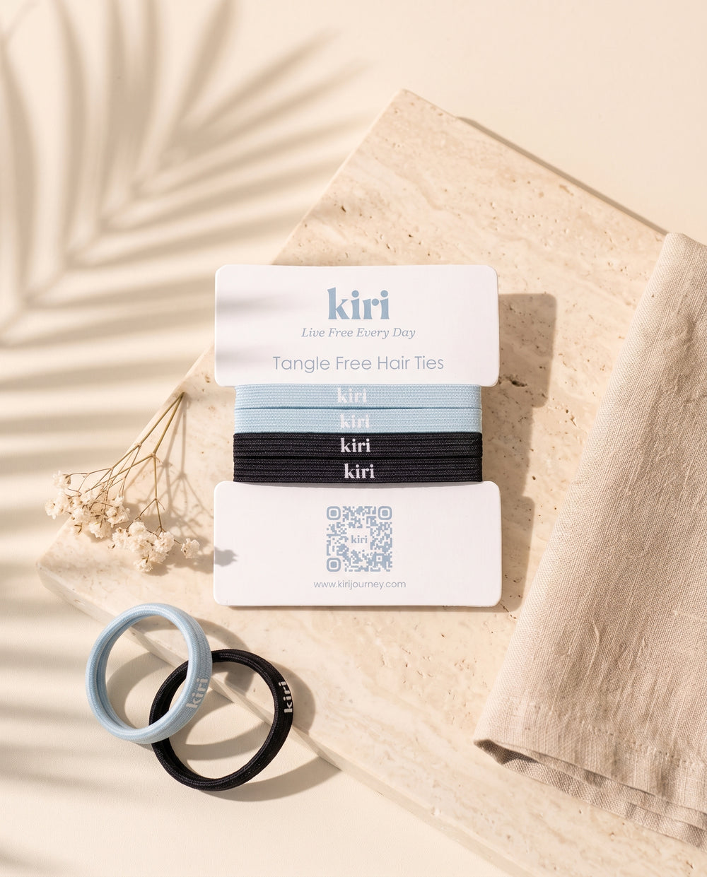 Kiri 防缠结发圈卡放在石灰华石上，旁有亚麻布和干花