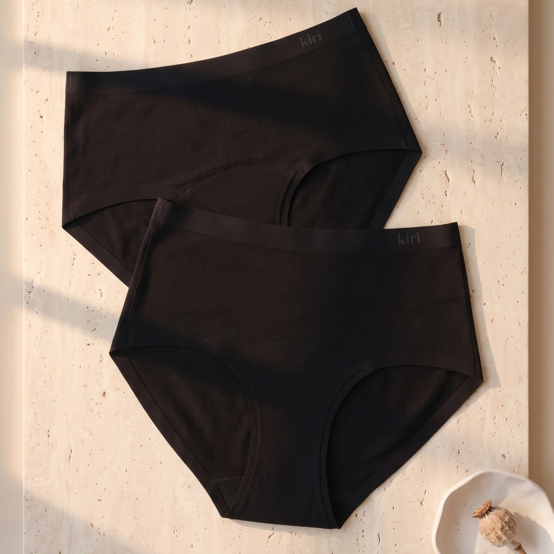 Two Kiri Selene Black nightwear period underwear, front view, on travertine