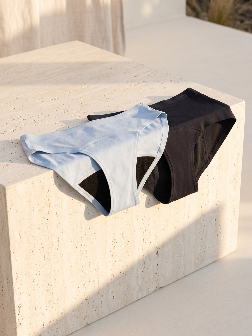 Kiri Celeste Blue daywear and Selene Black nightwear on a pale travertine block in afternoon sun