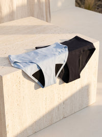 Kiri Celeste Blue daywear and Selene Black nightwear on a pale travertine block in afternoon sun 1