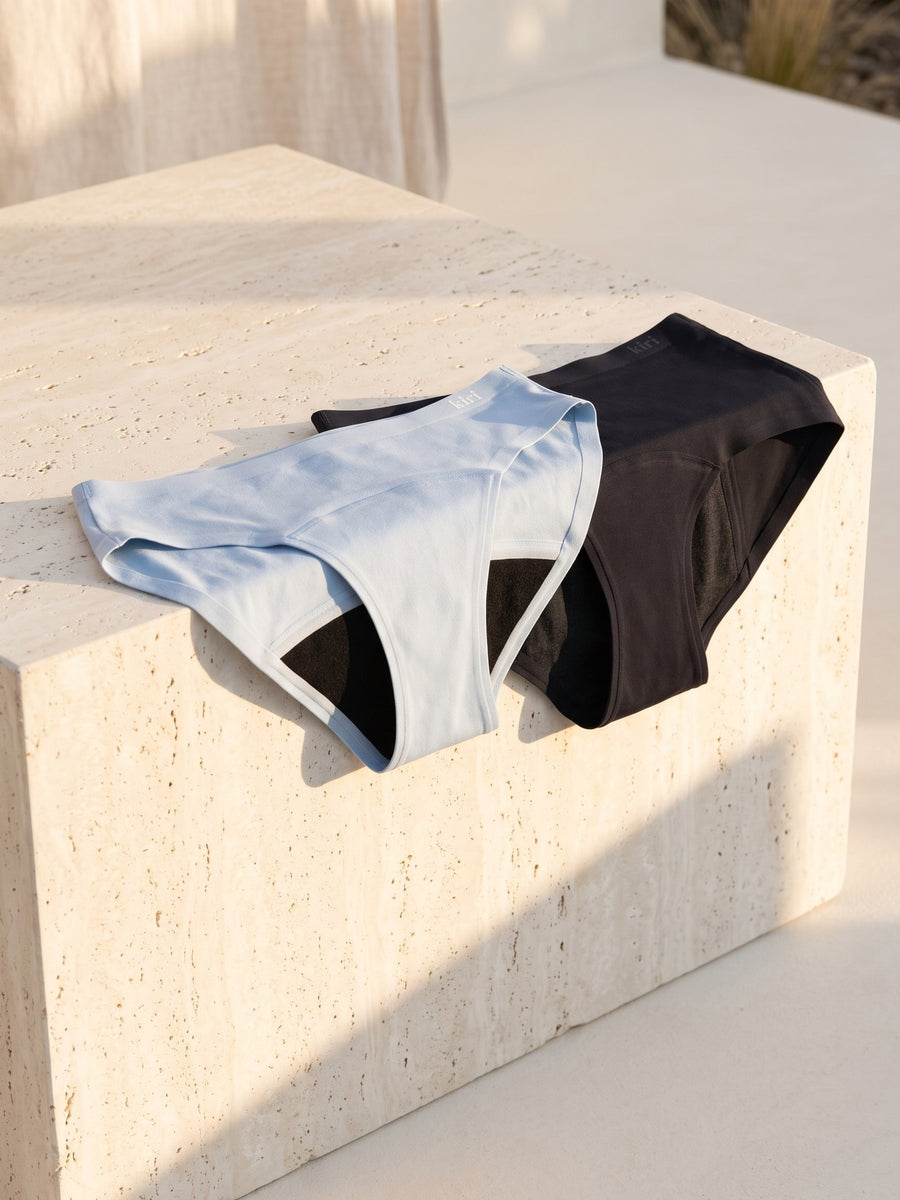 Kiri Celeste Blue daywear and Selene Black nightwear on a pale travertine block in afternoon sun