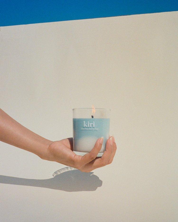 Hand holding the Kiri Live Free Every Day candle against a blue sky